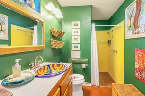 A bathroom with a green wall, a white sink, a mirror, a shower curtain, and a toilet. - Charming 2 bedroom cottage with private pool in the heart of the Texas Hill Coun (Johnson City)