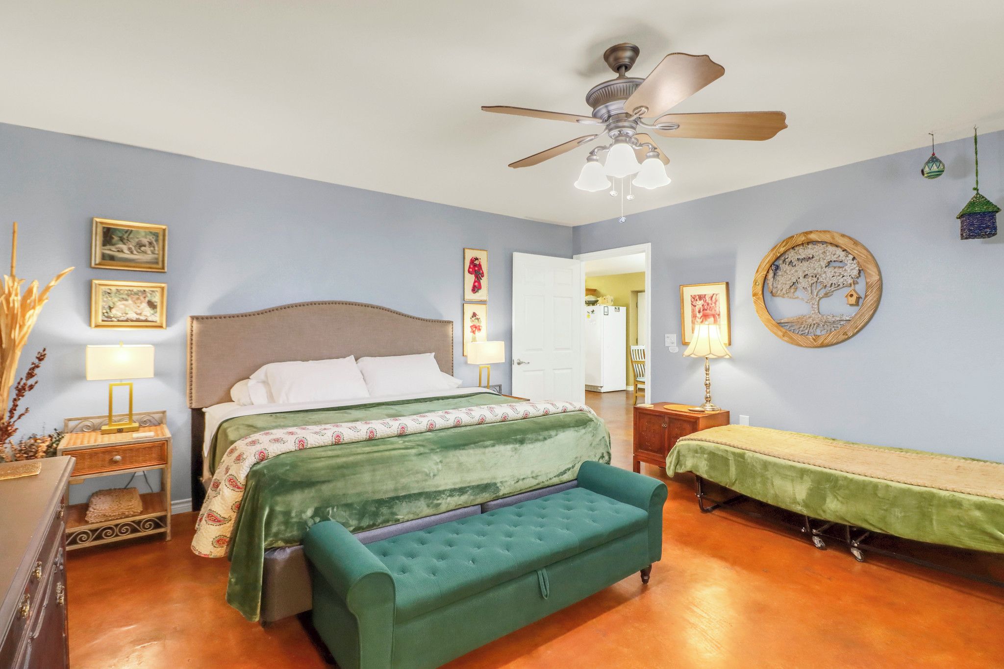 Une chambre à coucher avec un lit, un canapé vert, un ventilateur de plafond et des décorations murales.