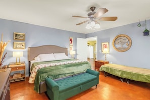 A bedroom with a bed, a green sofa, a ceiling fan, and wall decorations.