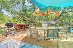 A wooden deck with a table and chairs, a hammock, a grill, and a shaded area with a canopy.