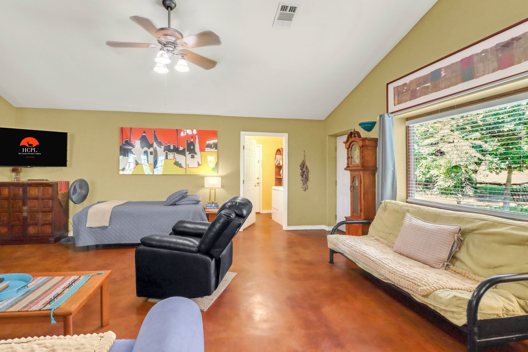 A room with a bed, a sofa, a chair, a television, and a ceiling fan.