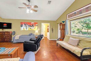 A room with a bed, a sofa, a chair, a television, and a ceiling fan.