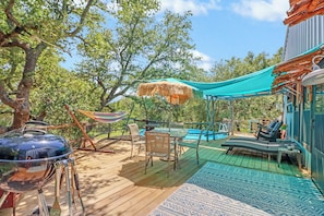 A wooden deck with a grill, outdoor furniture, a hammock, and a pool area.