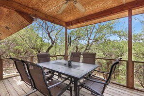 A covered outdoor patio with a table and chairs, wooden beams, and a view of trees. - Spacious 2/2 - ON the Cypress Creek with private hot tub! (Wimberley)