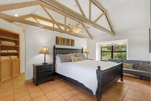 A bedroom with a large bed, a nightstand, a wooden wardrobe, a window with a view, and a ceiling fan. - Spacious 2/2 - ON the Cypress Creek with private hot tub! (Wimberley)