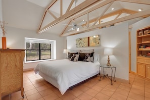 A bedroom with a large bed, a window, a ceiling fan, and a wooden cabinet.
