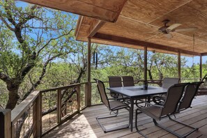 A covered outdoor patio with a table and chairs, surrounded by trees. - Spacious 2/2 - ON the Cypress Creek with private hot tub! (Wimberley)