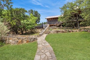 A stone pathway leading to a building with a large window and a staircase. - Spacious 2/2 - ON the Cypress Creek with private hot tub! (Wimberley)