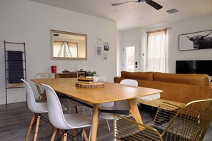 Una sala de estar moderna con una mesa de comedor de madera, sillas blancas, un sofá de cuero marrón y un televisor montado.