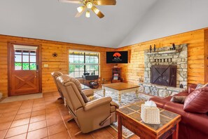 A log cabin interior with a fireplace, leather recliner, and a television mounted on the wall.