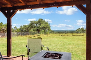 A covered patio with a metal chair and a table with a fire pit. - 3 bedroom pet friendly log cabin with private hot tub! (Wimberley)