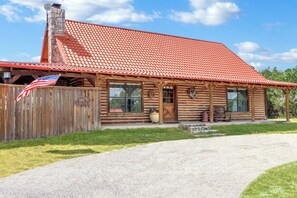 A log cabin with a red-tiled roof, a wooden fence, and an American flag.