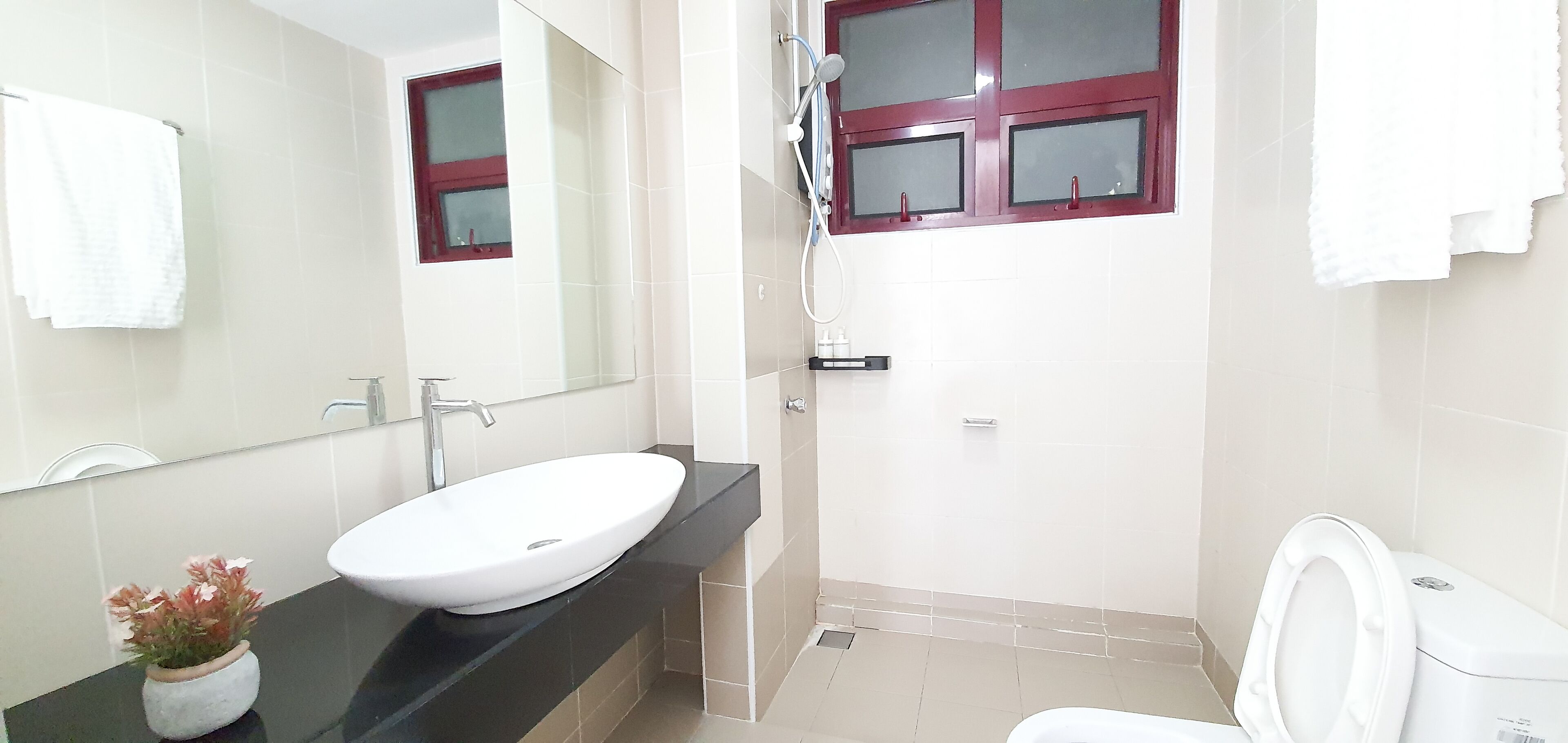 A bathroom with a white sink, a mirror, a window with a red frame, and a toilet.