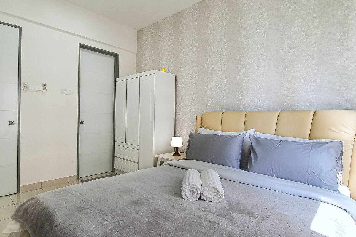 A bedroom with a bed, a nightstand, a lamp, a wardrobe, and a mirror.