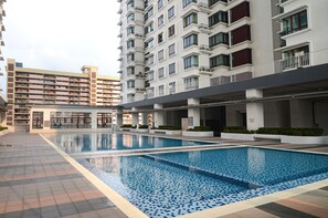 A swimming pool area with a tiled deck, a building with multiple balconies, and a modern architectural design. - Dahlia Home at Rafflesia Condominium (Kuala Lumpur)