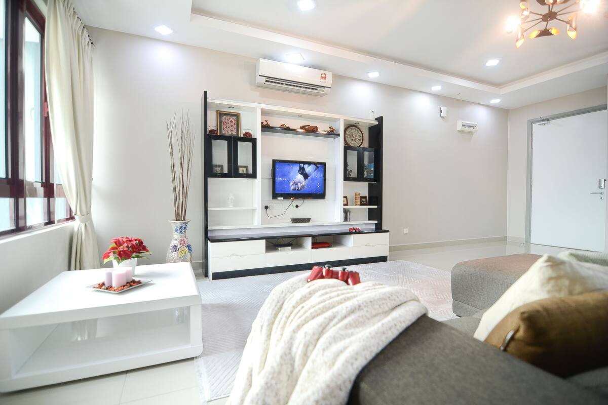 A modern living room with a flat-screen TV, white furniture, and decorative items.