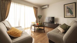 Een woonkamer met een bank, een salontafel met fruit en glazen, een televisie en een airconditioner.