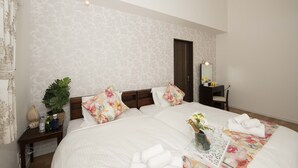 Een hotelkamer met een groot bed, bloemenkussens, een nachtkastje met een plant, een vaas met bloemen en netjes opgevouwen handdoeken.