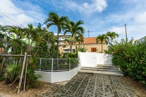 A residential area with a paved entrance, palm trees, and a building with a tiled roof. - Miyakojima Villa Charles (Miyakojima)