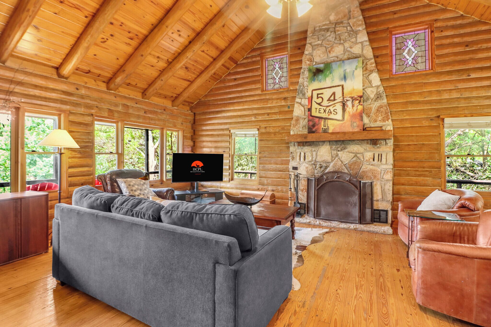 A log cabin interior with a stone fireplace, a television, and a sofa.