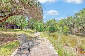 A bench by a river with trees and a clear sky. - Popular 2BR Log Home on the Creek with a Hot Tub! (Wimberley)