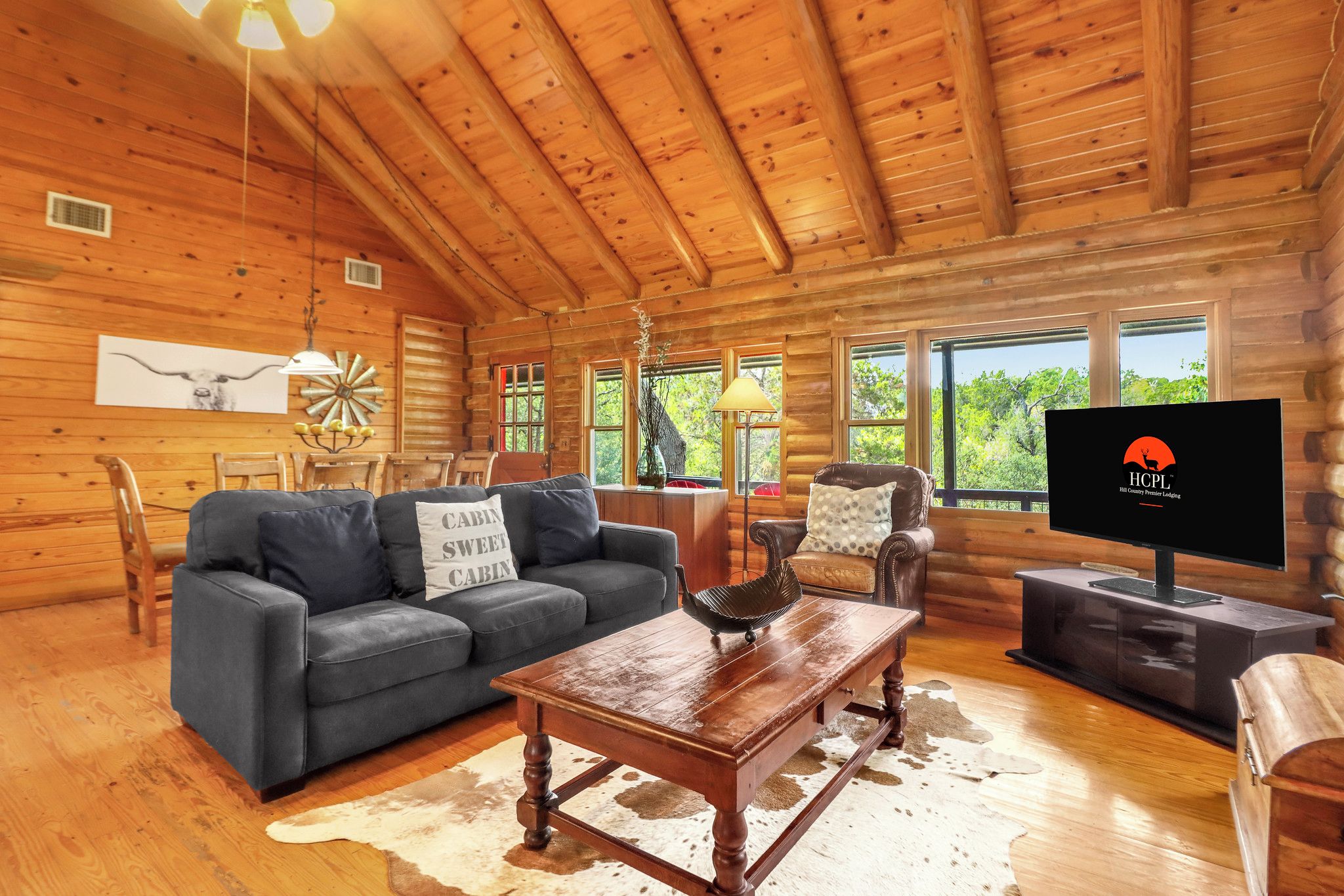 A log cabin interior with a sofa, a coffee table, a television, and a view of the outdoors.