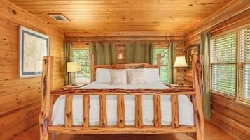A wooden cabin bedroom with a bed, two bedside lamps, and a window with blinds.