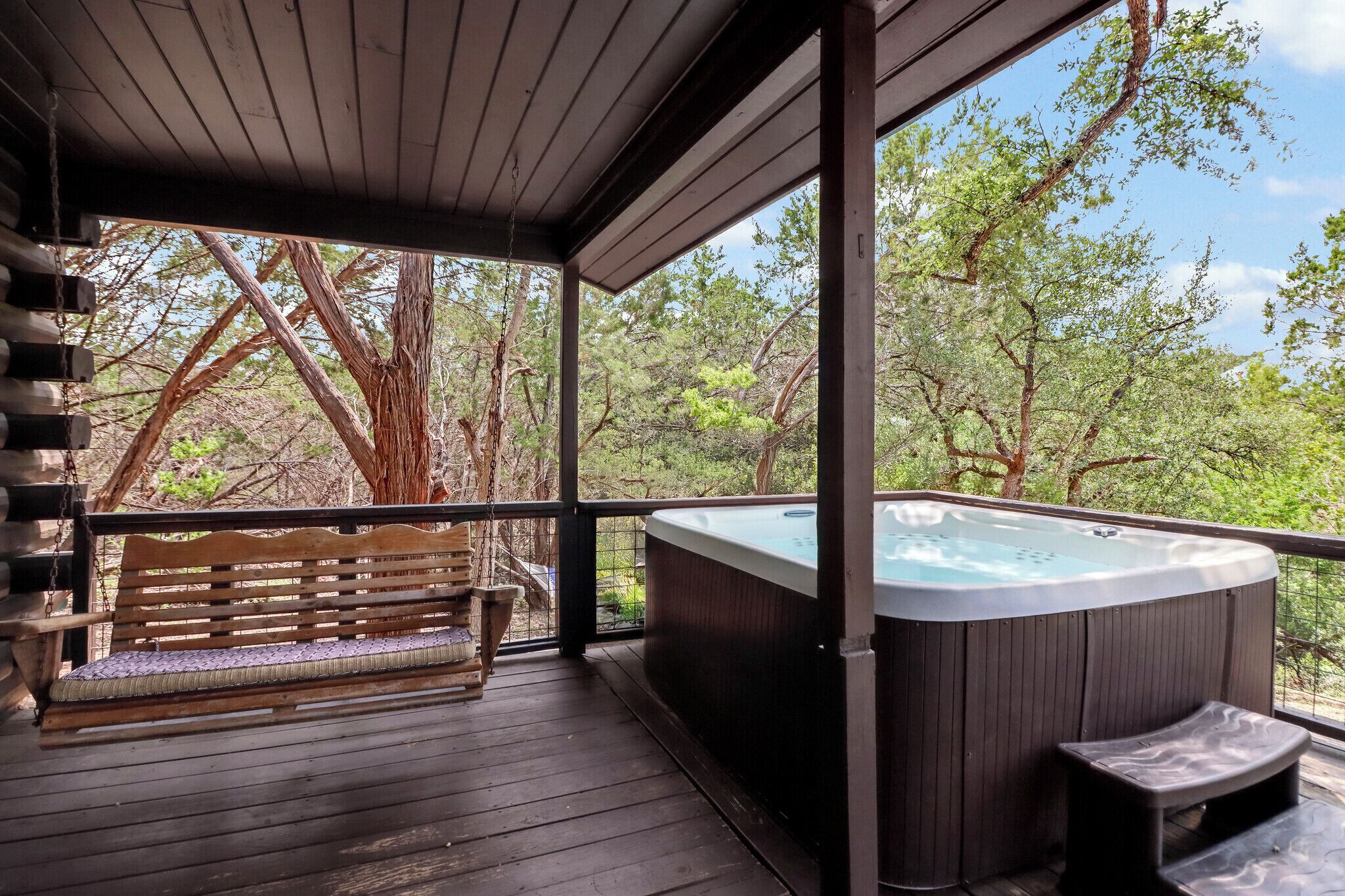 Eine Holzterrasse mit Whirlpool und Sitzbank, umgeben von Bäumen.