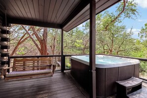 A wooden deck with a hot tub and a bench, surrounded by trees.