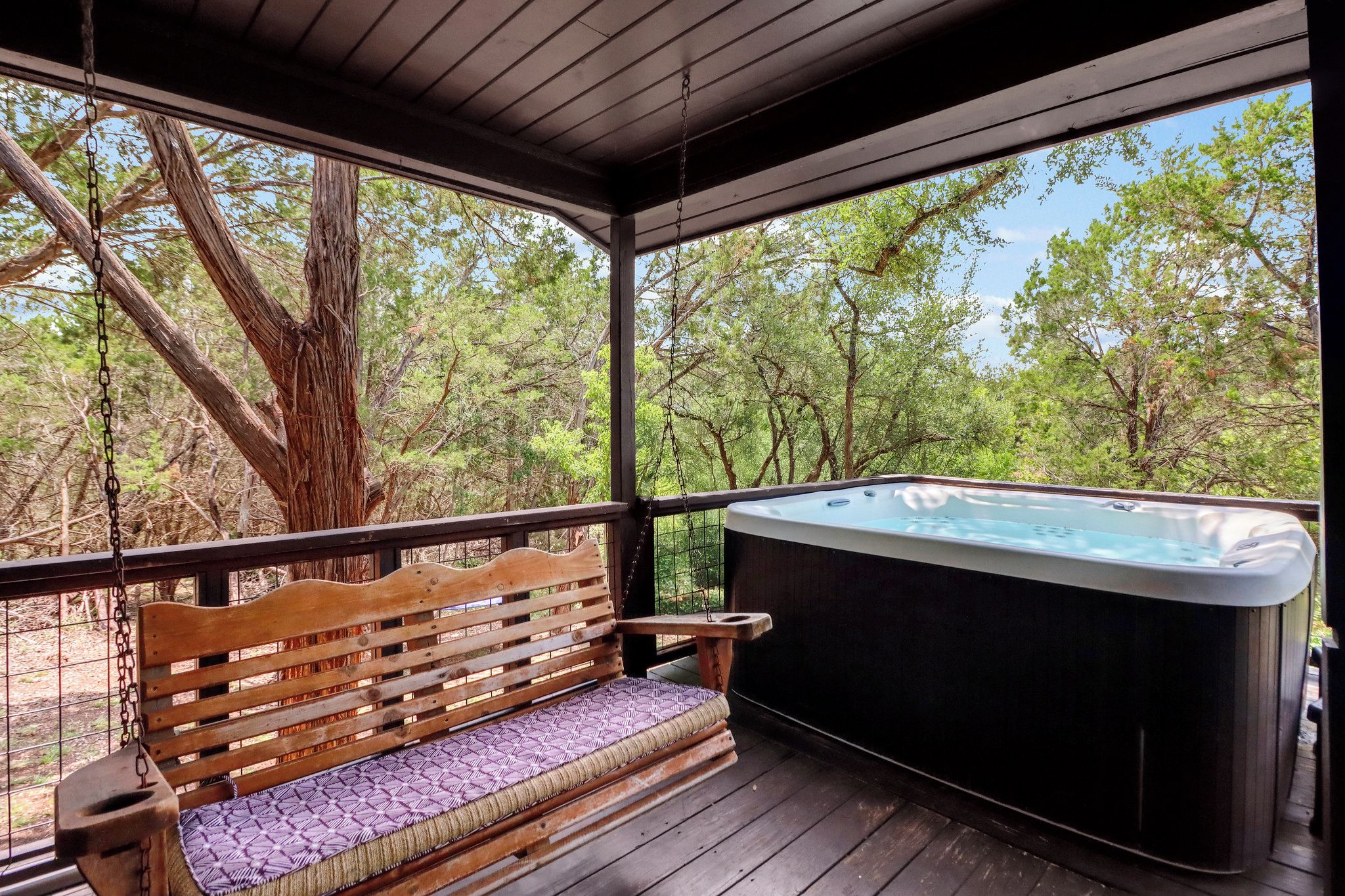 Un banc en bois avec un coussin, un jacuzzi et une vue sur les arbres.