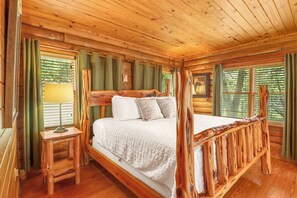 A wooden cabin bedroom with a four-poster bed, a nightstand, and a window with curtains.