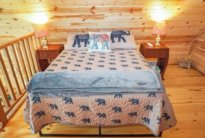 A wooden cabin bedroom with a bed, two nightstands, and a giraffe decoration. - Safari Treehouse w/ Fire Pit, Grill & Seasonal Creek Views in Dripping Springs (Wimberley)