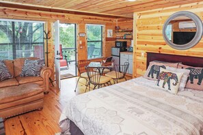 A cozy cabin with a wooden interior, a bed with patterned bedding, a dining area, and a small kitchenette. - Safari Treehouse w/ Fire Pit, Grill & Seasonal Creek Views in Dripping Springs (Wimberley)