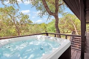 A hot tub on a wooden deck with a view of trees and sky. - Popular 2BR Log Home on the Creek with a Hot Tub! (Wimberley)