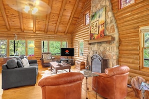 A log cabin interior with a fireplace, a television, and a stone wall.