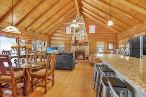 A log cabin interior with a dining area, living room, and kitchen.