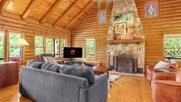 A log cabin interior with a stone fireplace, a television, and a sofa.