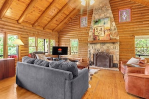 A log cabin interior with a stone fireplace, a television, and a sofa.