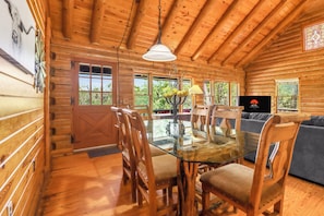 A wooden cabin interior with a dining area, a sofa, and a TV.