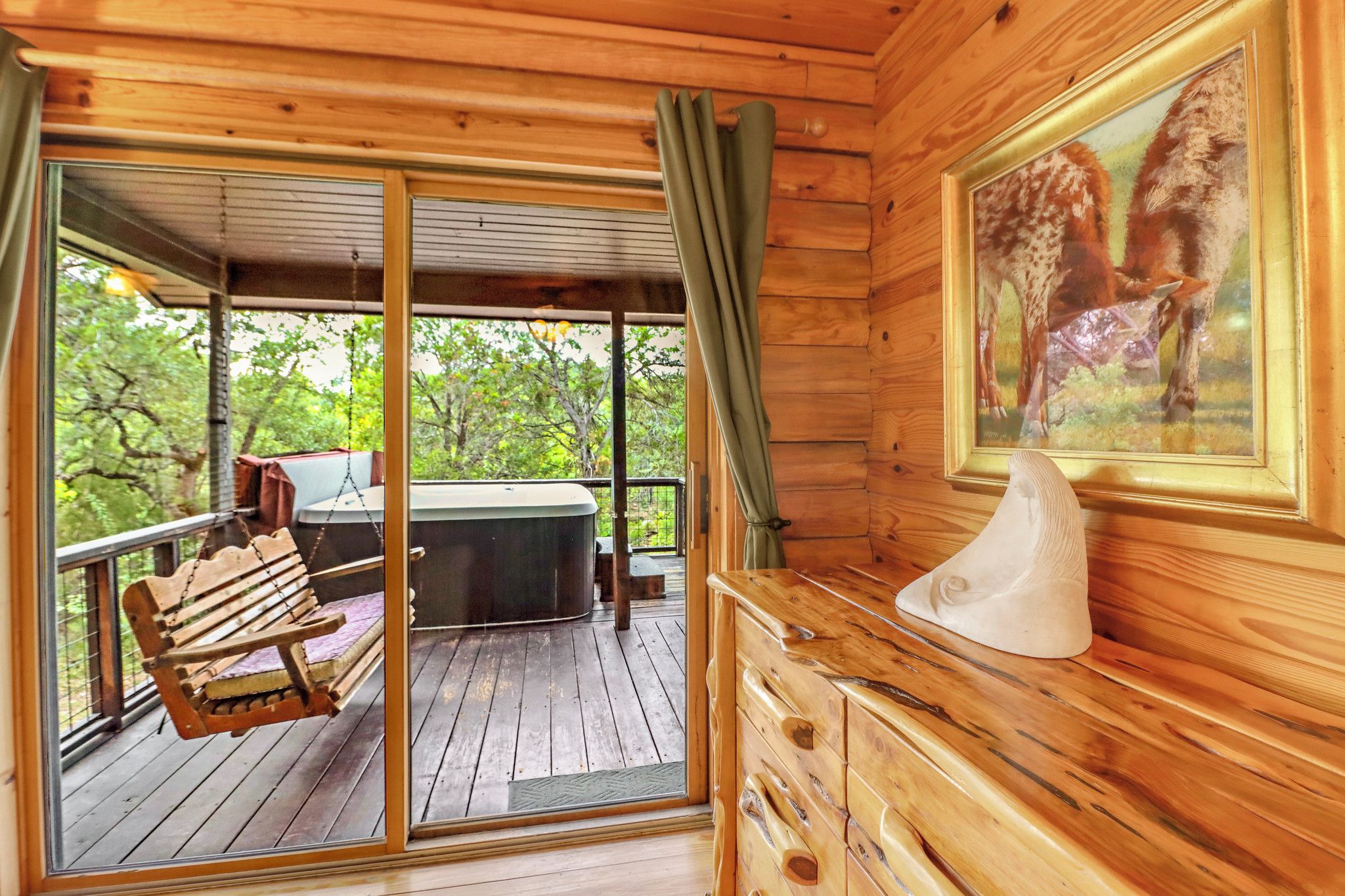 A wooden cabin with a deck, a bench, a hot tub, and a painting of a horse.