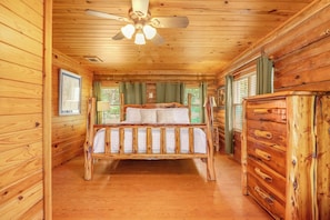 A wooden cabin bedroom with a bed, a dresser, and a ceiling fan.