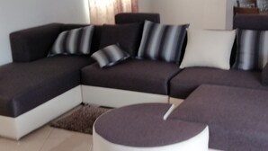 A modern living room with a sectional sofa, a round ottoman, and a small rug. - Private House for Rent in Mauritius at a very competitive Price and very secure. (Phoenix)