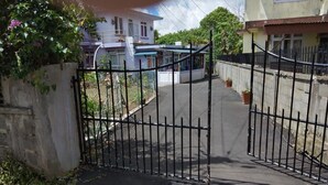 A gated driveway leading to a residential area with houses in the background. - Private House for Rent in Mauritius at a very competitive Price and very secure. (Phoenix)