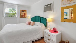 Un dormitorio con cama, mesita de noche, lámpara y un cuadro en la pared.