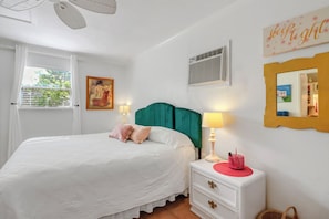 Un dormitorio con cama, mesita de noche, lámpara y un cuadro en la pared.