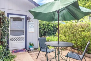 A patio with a round table and chairs, a green umbrella, and a white door with a window. - Darling cottage on the Blanco River. Minutes from downtown Wimberley! (Wimberley)