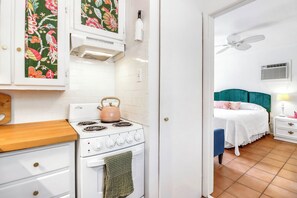 A kitchen with a stove and a kettle, a bedroom with a bed and a nightstand, and a bathroom with a shower. - Darling cottage on the Blanco River. Minutes from downtown Wimberley! (Wimberley)
