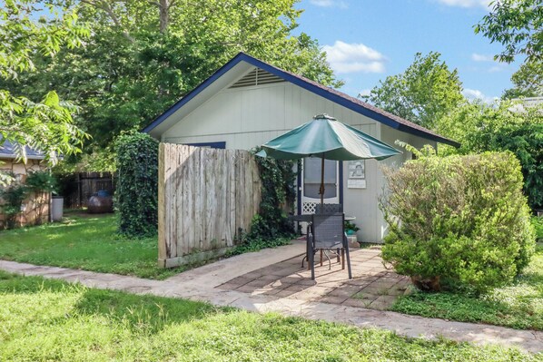 A small, single-story building with a covered patio area, a wooden fence, and a well-maintained lawn.