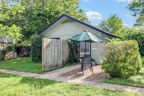 A small, single-story building with a covered patio area, a wooden fence, and a well-maintained lawn.