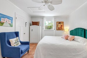 Un dormitorio con cama, una silla, armario, ventilador de techo, ventana y un cuadro.
